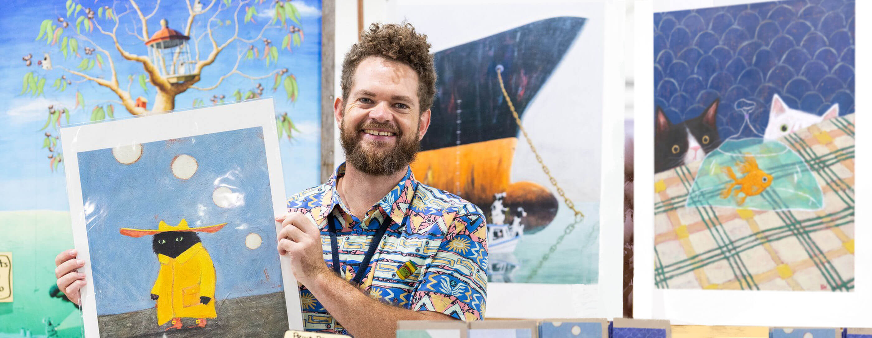 Australian Artist Beau Wylie holding a painting with various artworks in the background