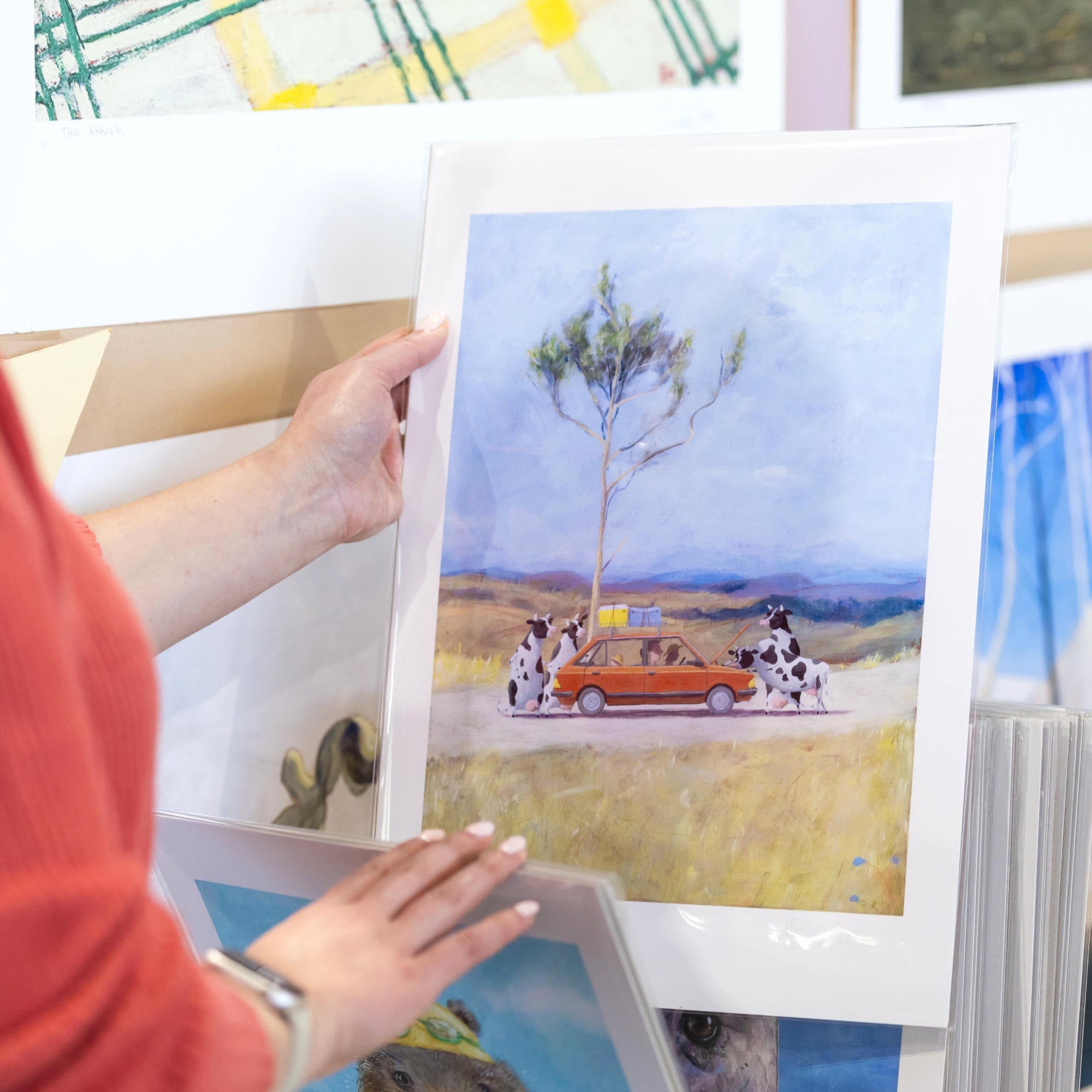 Person holding a framed artwork of a car and cows on a landscape.